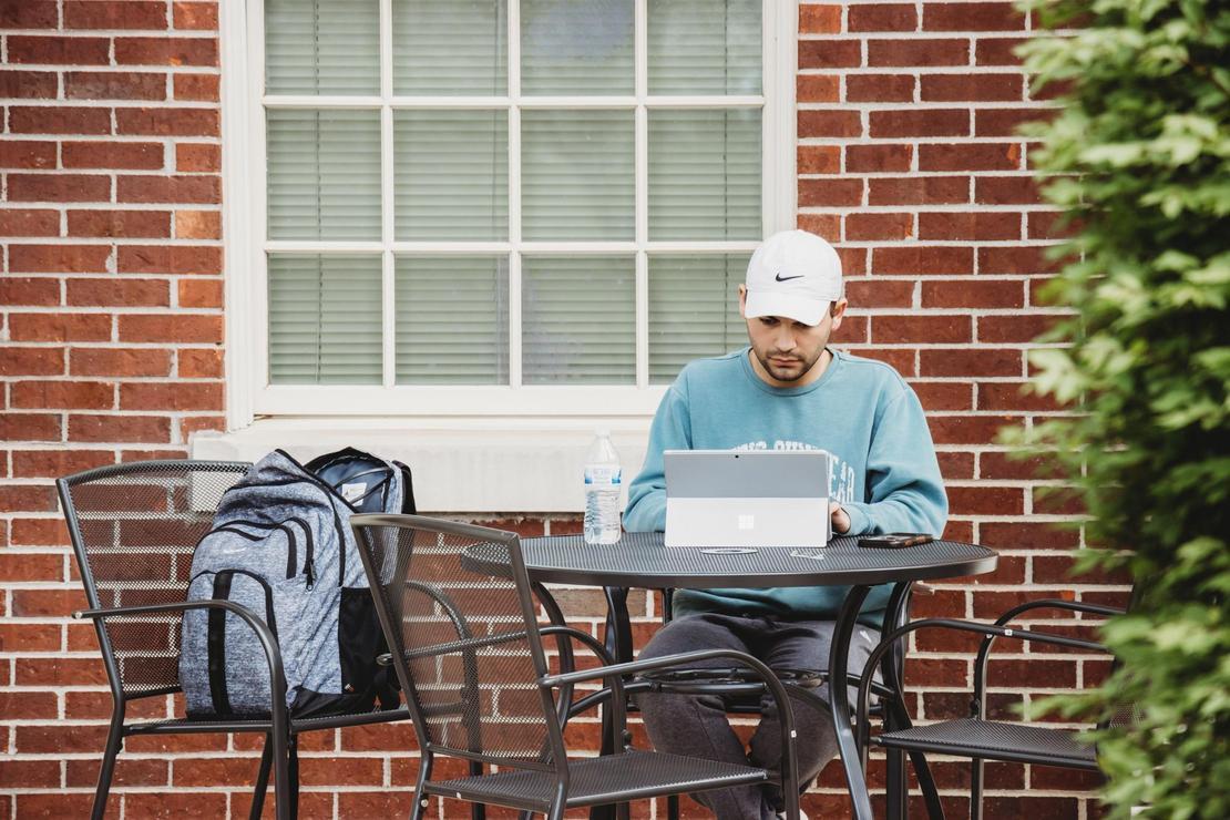 Student sitting at an outside patio working on college course work on his laptop